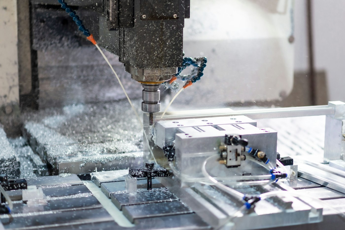 A CNC milling spindle cutting an aluminum part in a vise, with chips across the machine bed